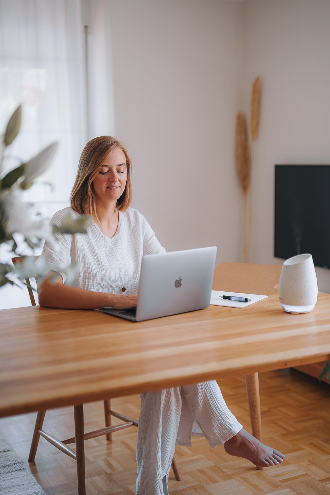 Stefanie Ensenberger sitzt an einem Holztisch am Laptop in einem hellen Wohnzimmer