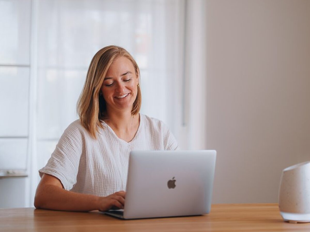 Stefanie Ensenberger sitzt lächelnd am Holztisch vor ihrem Laptop