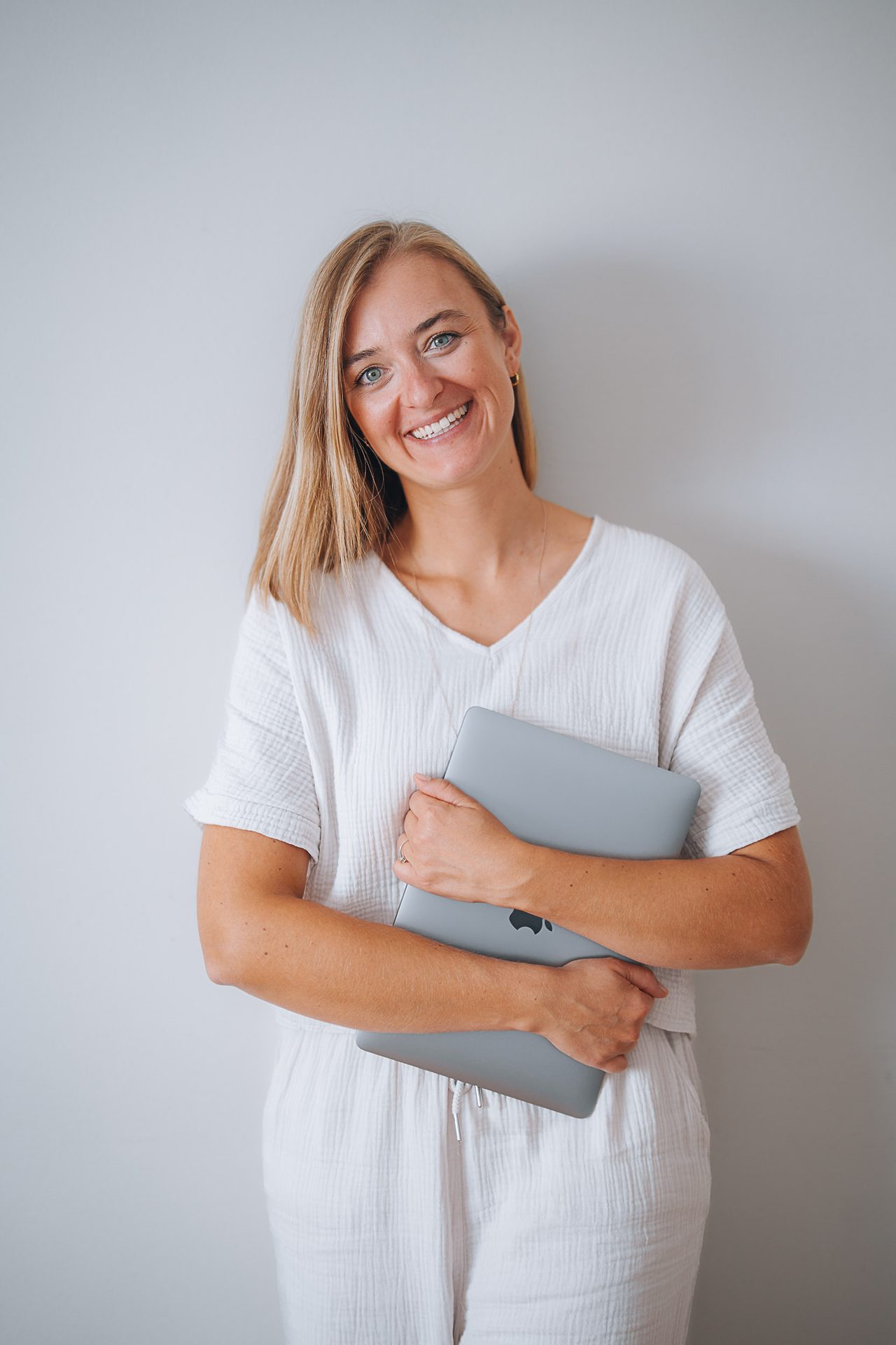 Stefanie Ensenberger steht lächelnd vor einer hellen Wand und hält einen Laptop im Arm